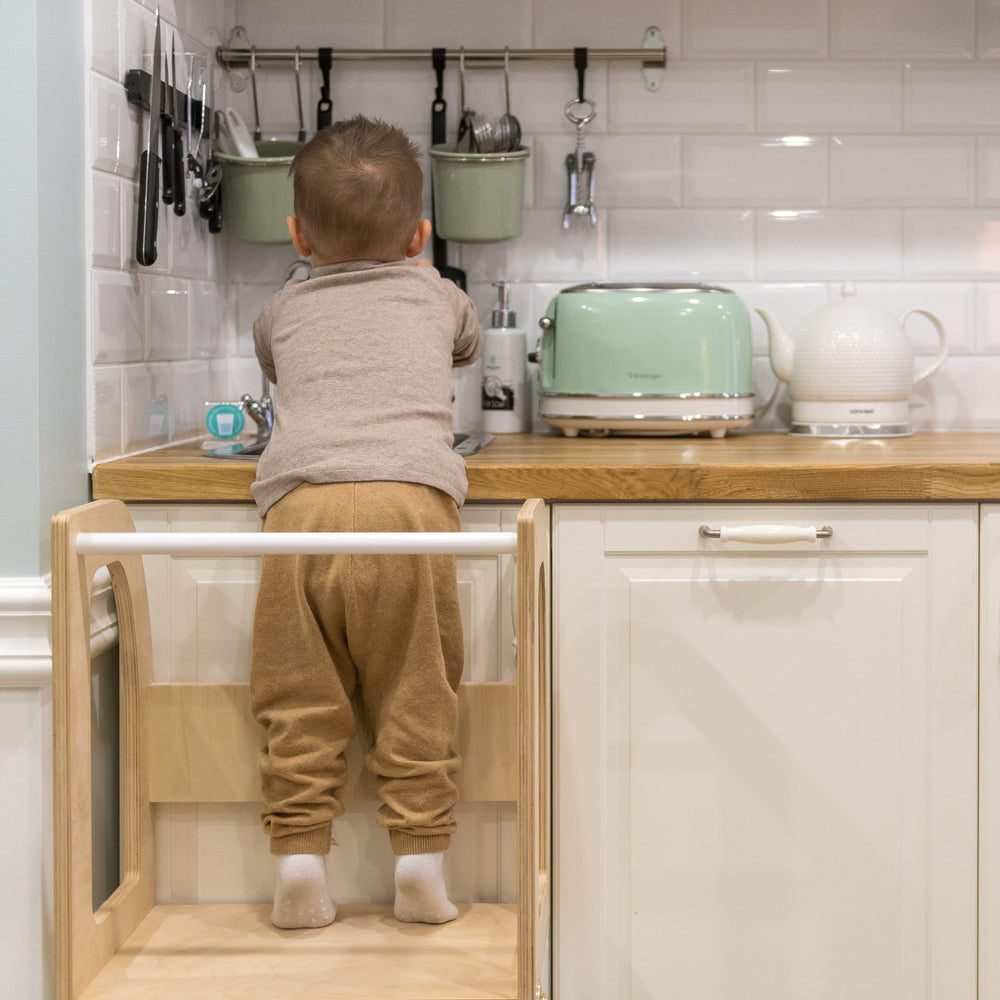 Kind auf höhenverstellbarem 2in1 Lernturm in gelbem Kinderzimmer beim sicheren Entdecken der Küche Sitzmöbel für Kinder Spiel & Bewegung Kinder