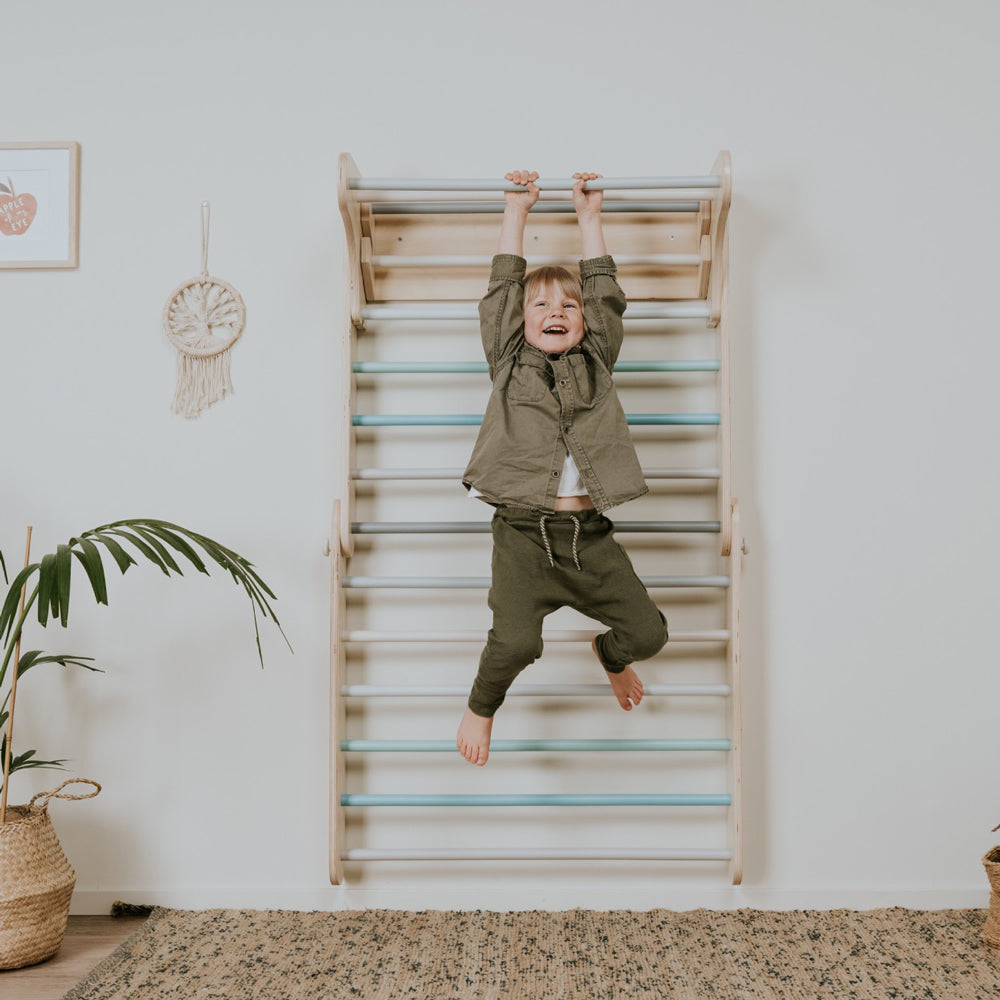 Kind klettert fröhlich an 2in1 Kletterdreieck und Sprossenwand aus Holz in sanften Pastellfarben für spielerische Bewegung.