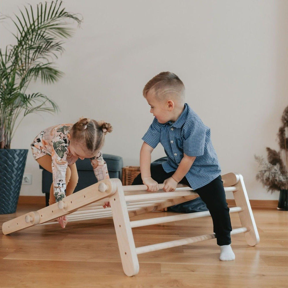 Zwei Kinder spielen begeistert mit dem natürlichen Pikler Kletterdreieck 4-teilig mit Rampe im Wohnzimmer, fördert Spiel & Bewegung Kinder.
