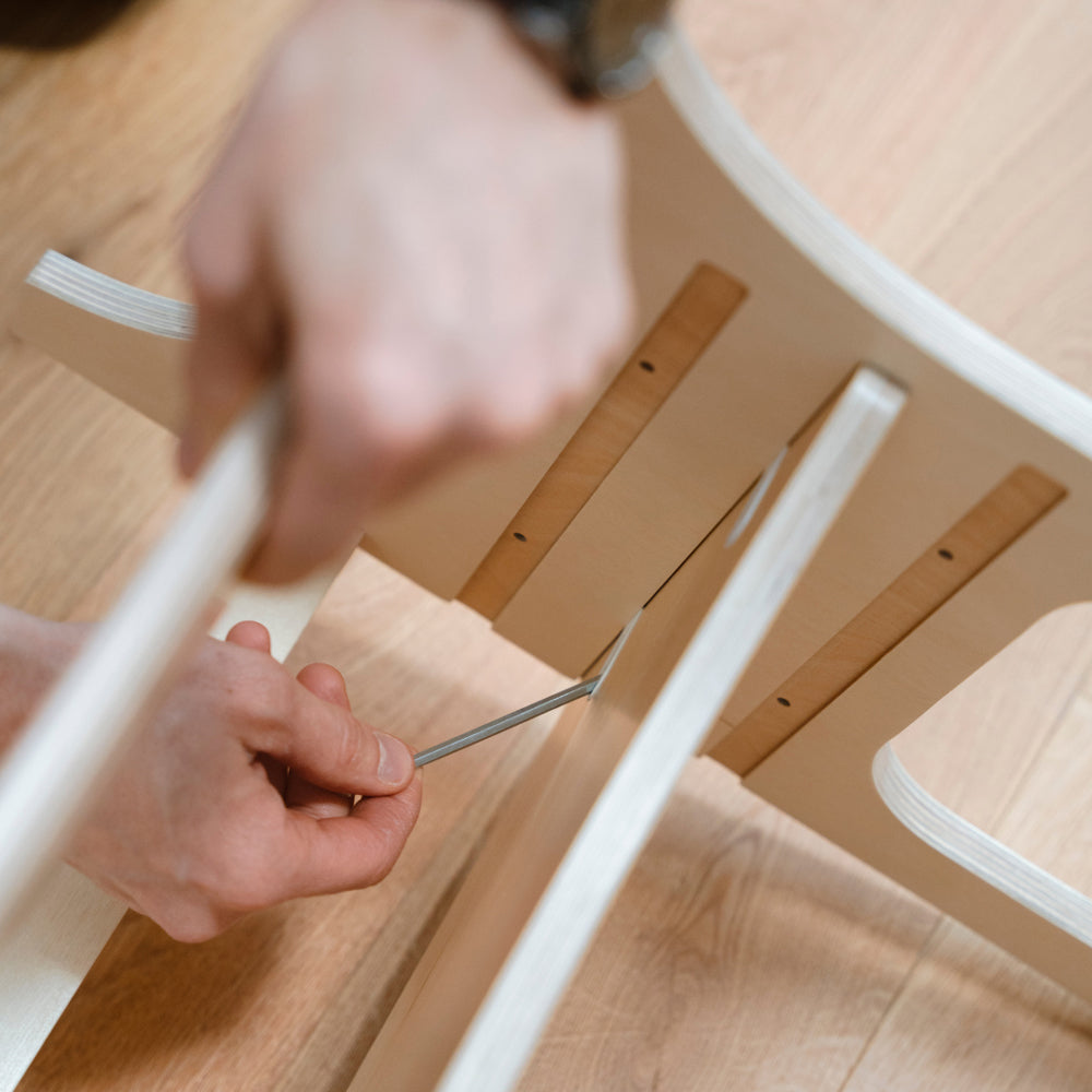 Man schraubt den höhenverstellbaren Tritthocker aus Birkensperrholz mit einem Schraubenzieher zusammen.