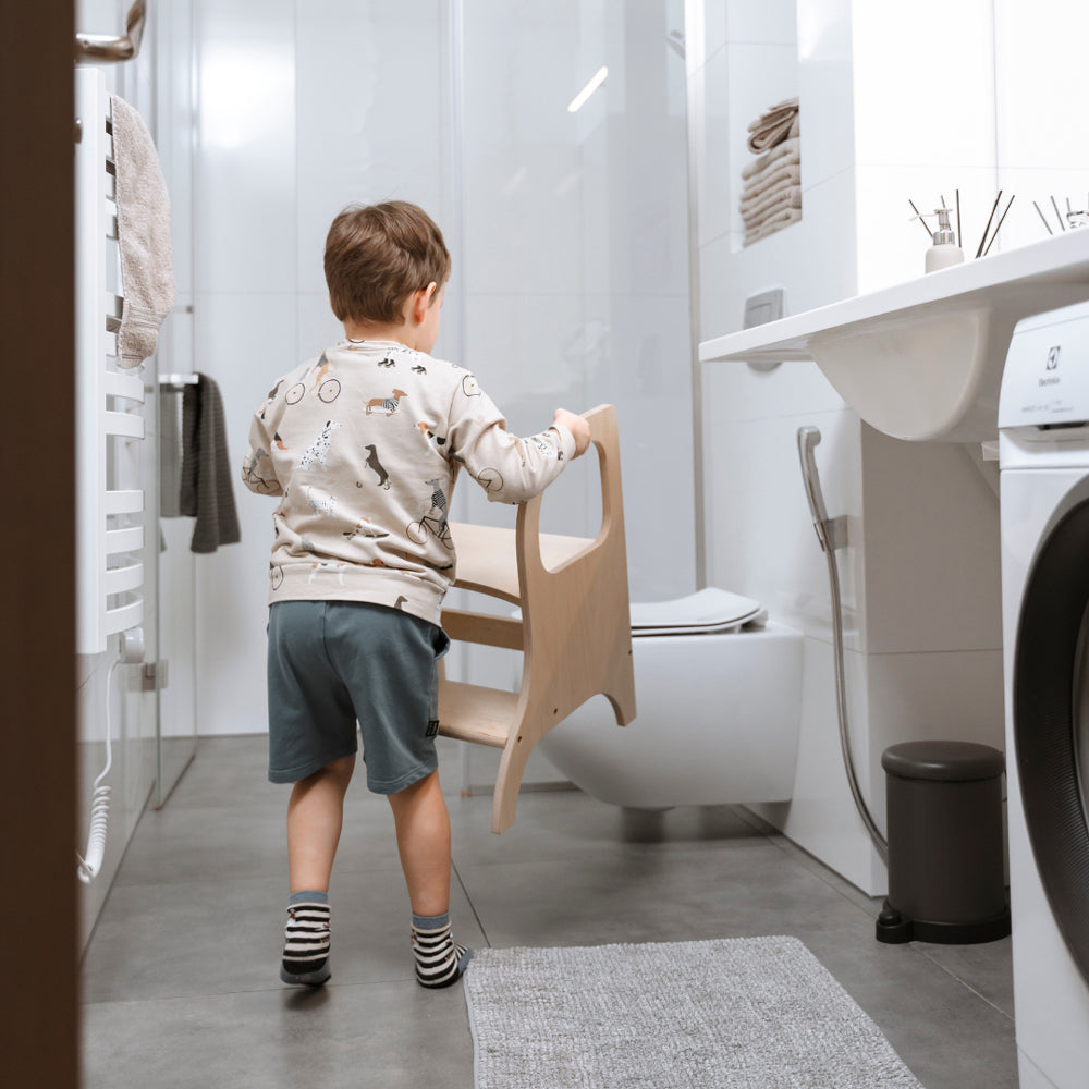 Kleines Kind trägt höhenverstellbaren Tritthocker aus naturfarbenem Birkensperrholz im modernen Badezimmer für mehr Selbstständigkeit.