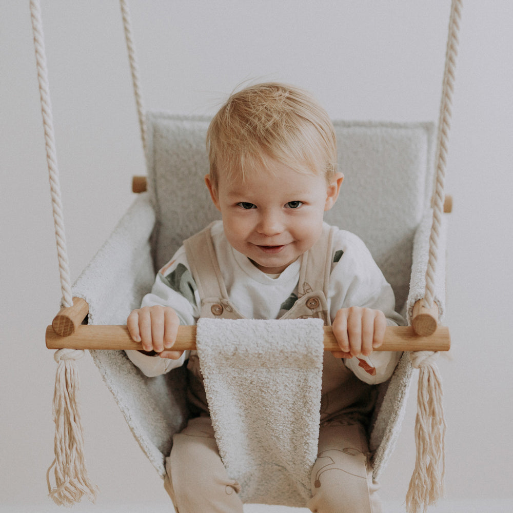Kleinkind sitzt in hellgrauer Babyschaukel Swing Boucle für Innenbereiche aus der Kollektion Spielzeug & Spiele, Fahr- und Wippspielzeug Kinder Neu