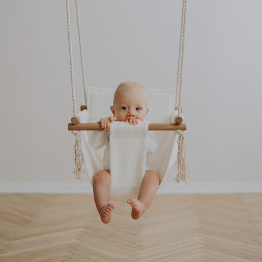 Baby sitzt glücklich in weißer Babyschaukel Swing Boucle für Innenbereiche aus Spielzeug & Spiele, Wipp- & Schaukelspielzeug Neuheiten.