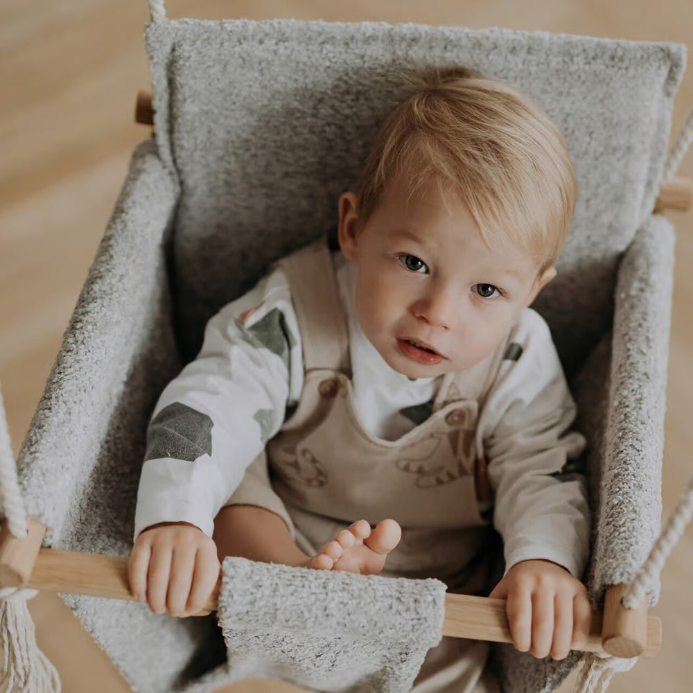 Kleines Kind sitzt in der Babyschaukel Swing Boucle grau, ideal für Spiel & Bewegung Kinder und Wipp- & Schaukelspielzeug Innenbereiche.