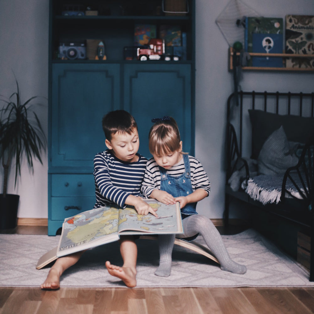 Zwei Kinder sitzen auf einem Balance Board aus Holz mit Filz und lesen gemeinsam ein Buch im gemütlichen Kinderzimmer aus der Spiel & Bewegung Kinder Kollektion.