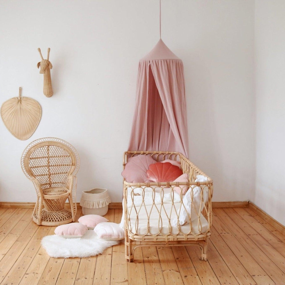 Rosa Betthimmel aus Bio-Baumwolle über einem Kinderbett aus Rattan, gemütlich und nachhaltig für das Kinderzimmer.