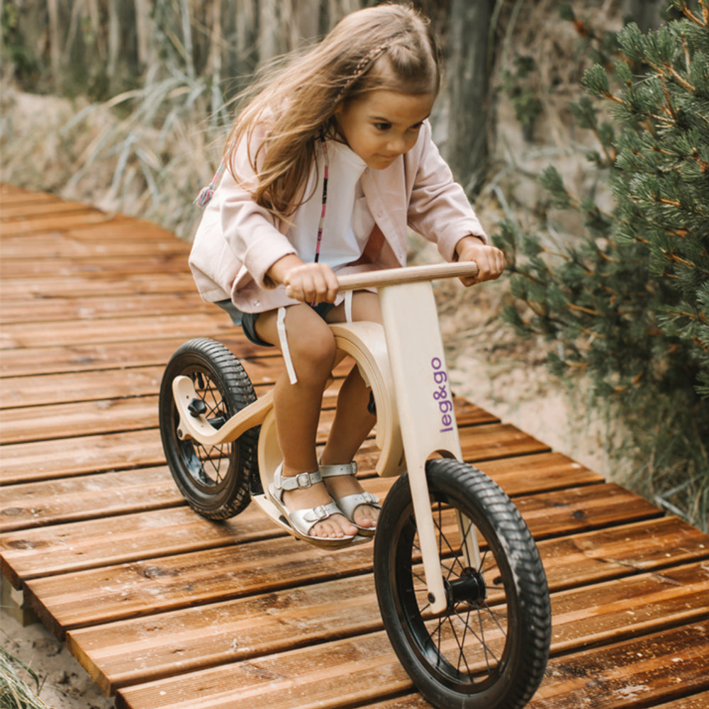 Kind fährt begeistert auf dem Laufrad modular & umbaubar 3in1 mit natürlichem Holzdesign auf einem Holzweg im Freien.