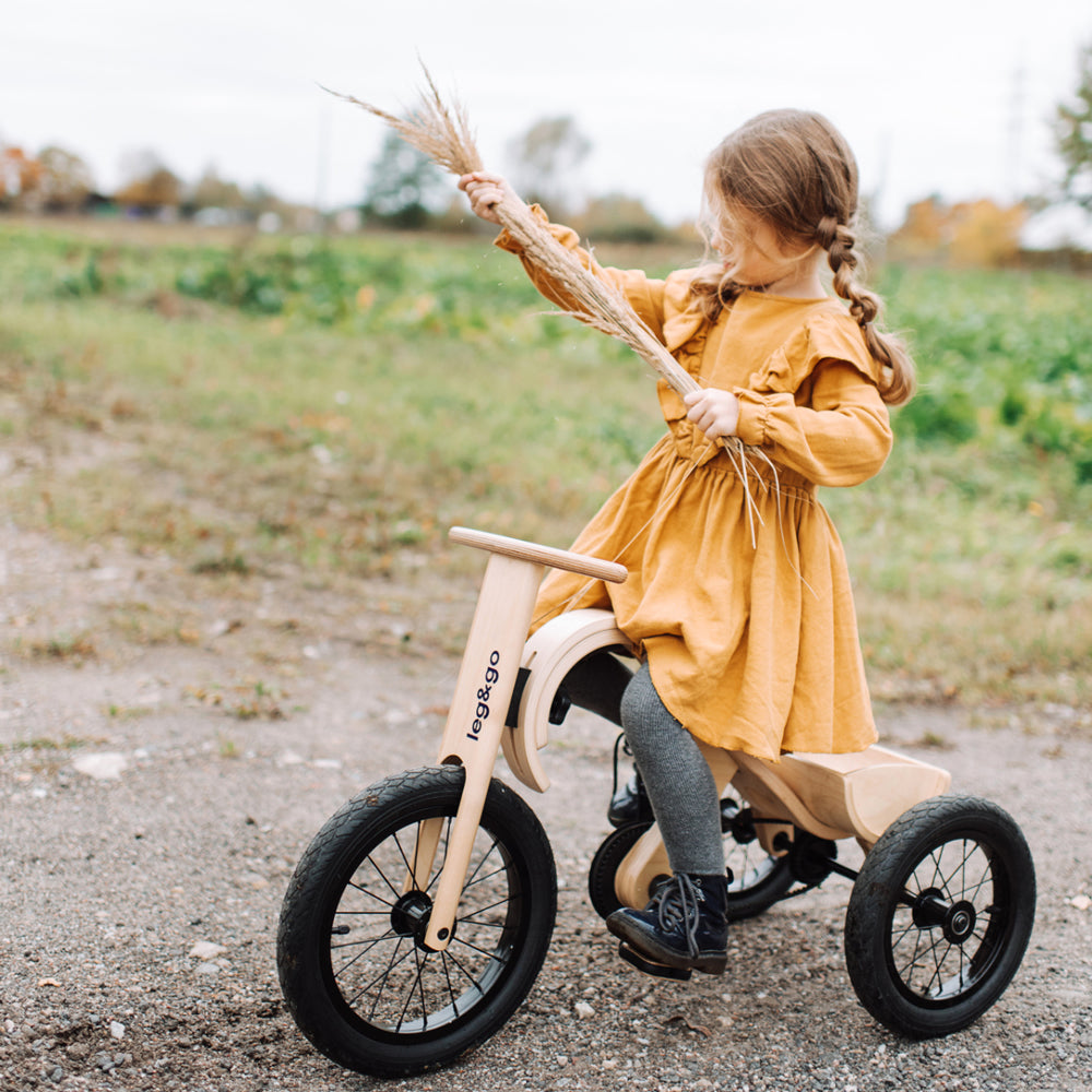 Kind auf naturfarbenem Dreirad Erweiterungsset im Freien, spielerisch Balance und Koordination lernen beim Fahren und Erkunden.