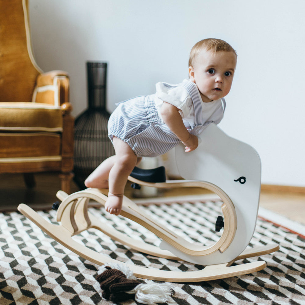 Kleines Kind spielt auf einem modernen, natürlichen Schaukelelefanten aus Holz im gemütlichen Wohnzimmerumfeld.