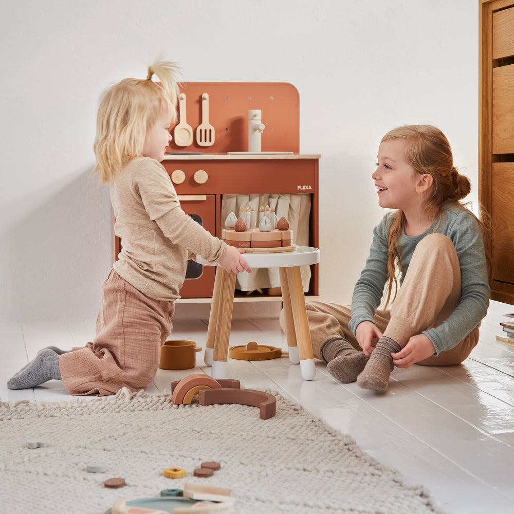 Zwei Kinder spielen mit dem Geburtstagskuchen-Spielset aus Holz für Kinderküchen, 25 Teile, fördern Fantasie und soziale Fähigkeiten spielerisch.