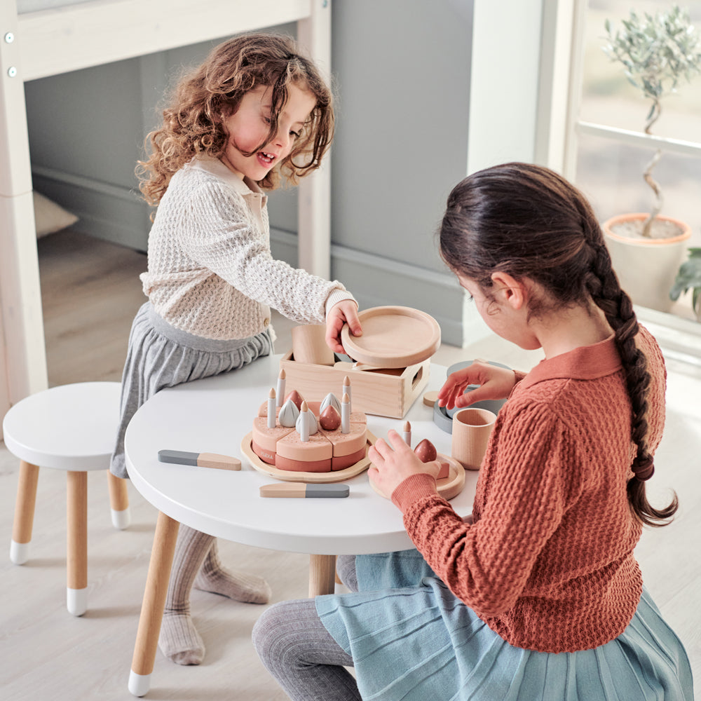 Zwei Mädchen spielen mit dem Geburtstagskuchen-Spielset aus Holz für Kinderküchen, 25 Teile, und gestalten eine fantasievolle Feier.