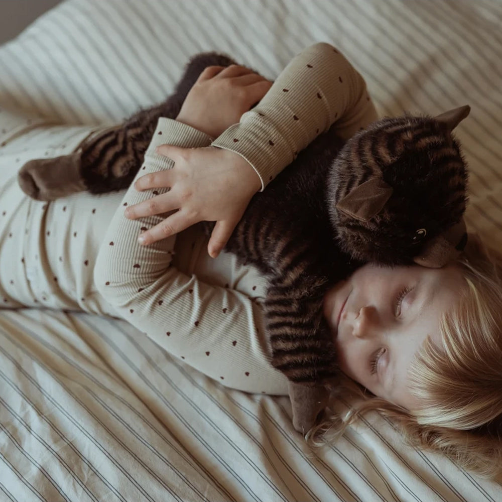 Kind liegt entspannt im Bett und hält eine gewichtete Kuscheltier Plüschkatze aus der Spielzeug & Spiele Kollektion fest.