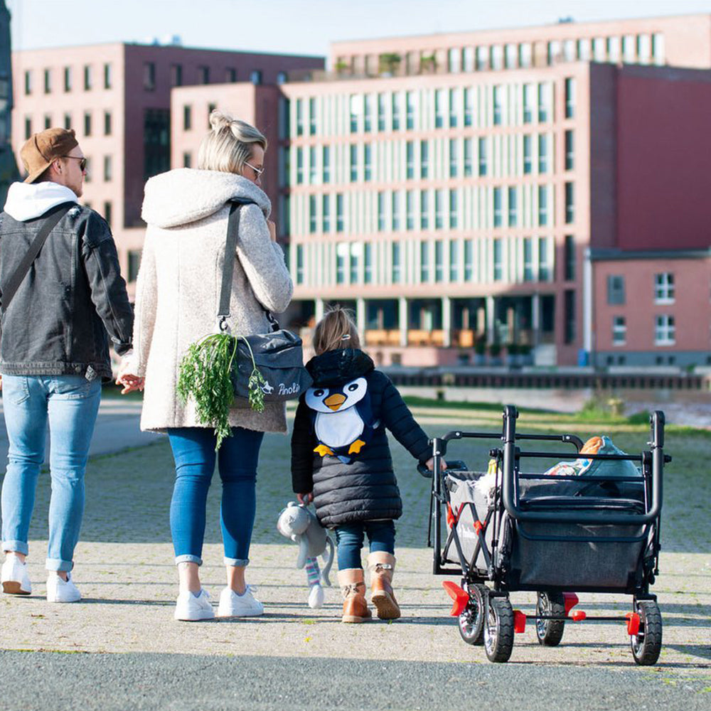 Familie spaziert mit klappbarem Bollerwagen mit Bremse und Sonnendach im urbanen Umfeld, perfekt für Spiel & Bewegung Kinder und Geschenke.