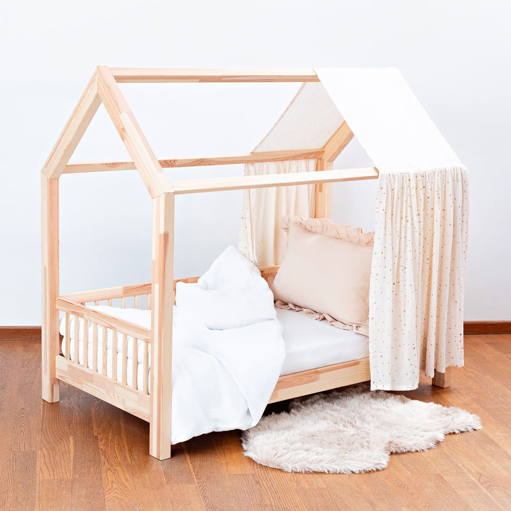 Kinderbett mit hellem Holzrahmen, weichen Kissen und einseitigem Musselin-Himmel mit goldenen Akzenten für gemütliche Momente im Kinderzimmer.