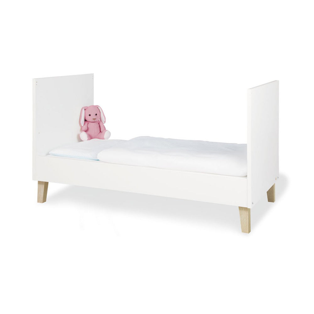 Weißes Babybett Lumi 70x140 cm mit höhenverstellbarer Funktion, aus der Babymöbel Neu Kollektion, mit weichem rosa Plüschtier dekoriert.