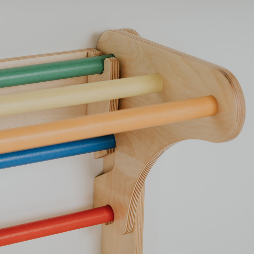 Nahaufnahme einer stabilen Holz-Sprossenwand mit bunten Stangen in Regenbogenfarben für Kinderzimmer und motorische Förderung.