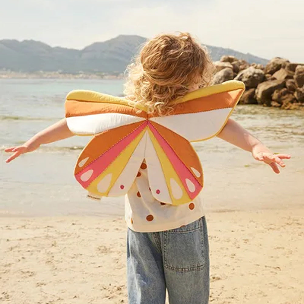 Kind trägt bunte Schmetterlingsflügel am Strand, ideal für Kinder von 3-5 Jahren aus der Blumenwiese Themenwelt Spielzeug & Spiele Kollektion.