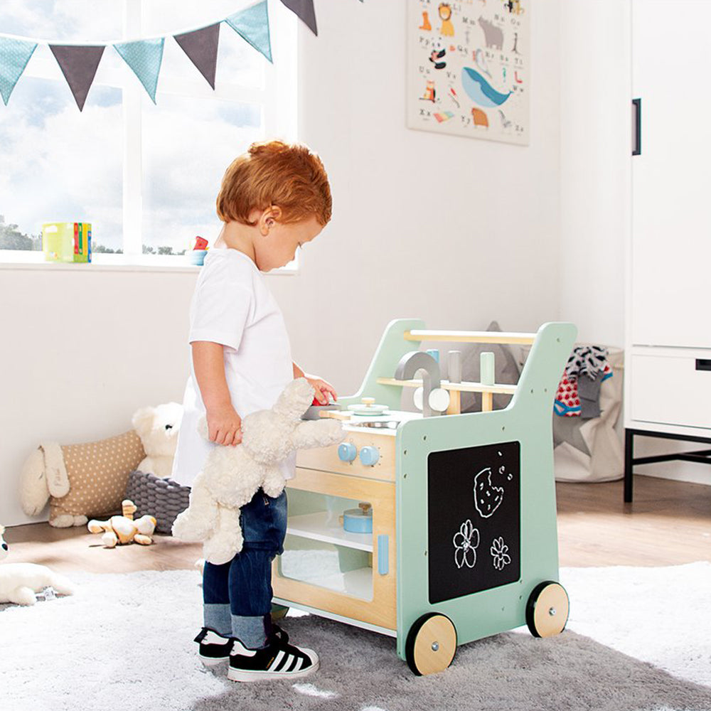 Kind spielt mit rollbarer Spielküche aus der Spielmöbel-Kollektion für Kinder in einem hellen, freundlichen Zimmer mit Spielzeug & Spiele.