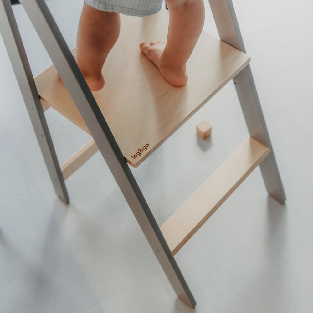 Kind steht sicher und selbstständig auf klappbarem, höhenverstellbarem Lernturm aus Holz aus der Spielmöbel Kollektion Pikler & Montessori.