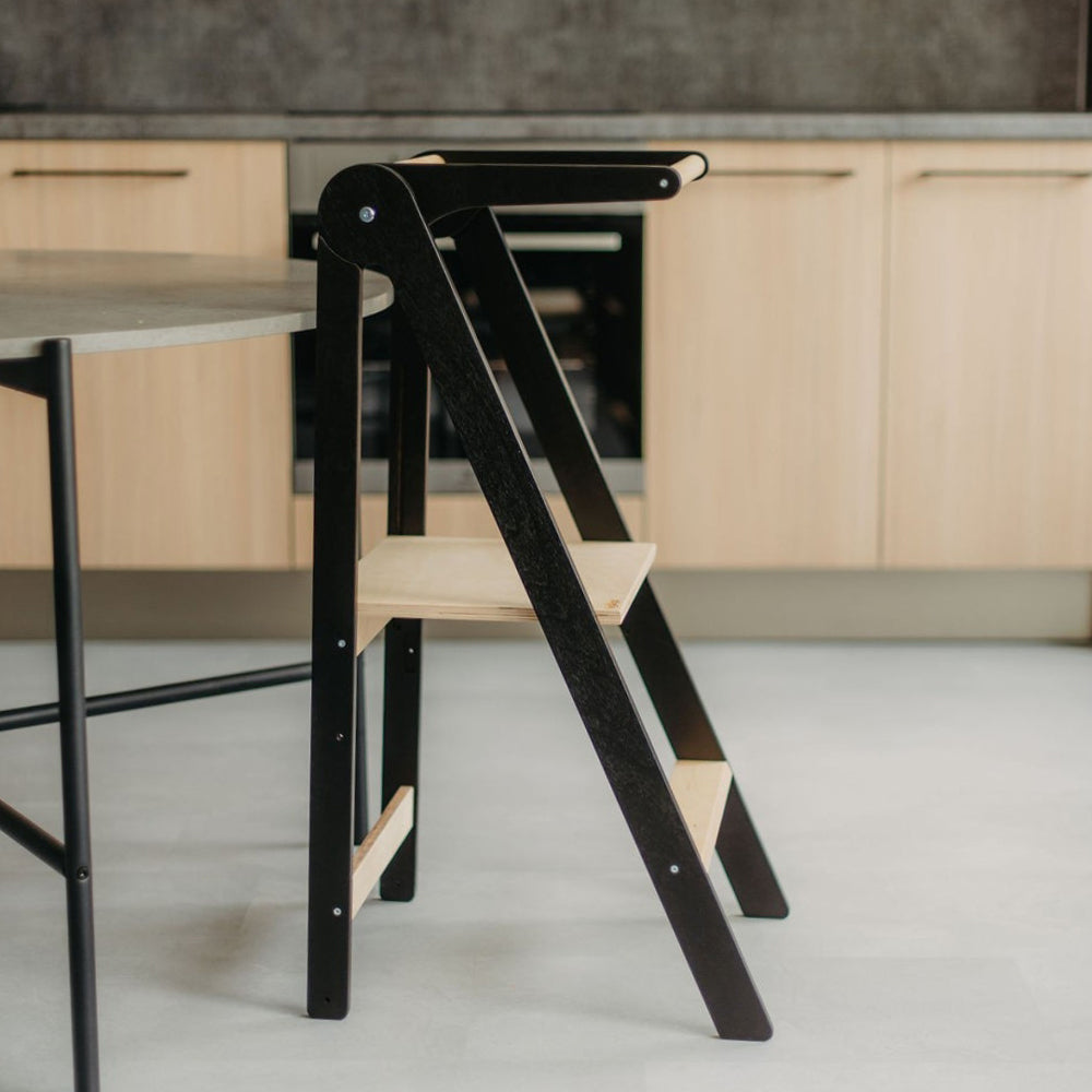 Klappbarer Lernturm aus Holz mit höhenverstellbaren Stufen und abnehmbarer Sicherheitsschiene aus der Spielmöbel Montessori Kollektion.