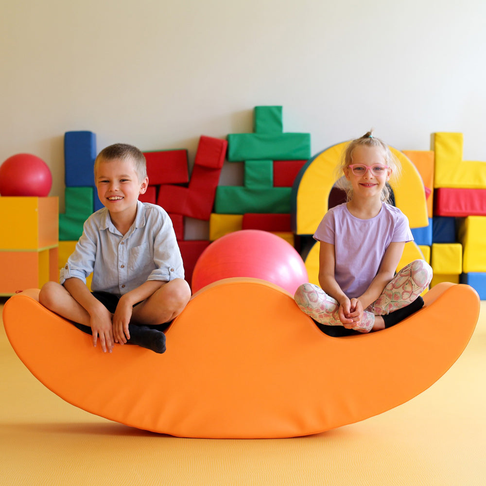 Zwei Kinder sitzen fröhlich auf einem orangefarbenen Softblock Wippe Rocker in der Kategorie Spielzeug & Spiele, Softblöcke & Bausteinsets.
