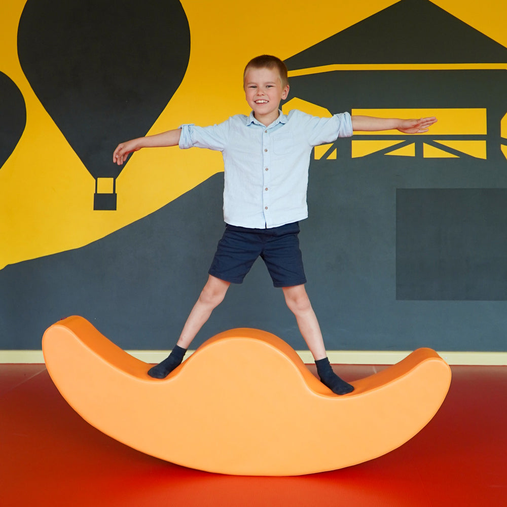 Kind spielt fröhlich mit orangem Softblock Wippe als Motorikspielzeug aus der Kategorie Spielzeug & Spiele für Kinder.