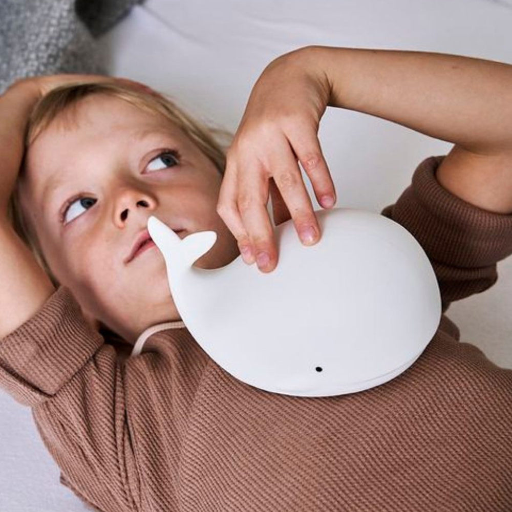 Kind liegt entspannt mit weißem Wal-Nachtlicht aus Silikon, leuchtet in 7 Farben, ideal als Kinderzimmer Deko und Beleuchtung für Kinder.