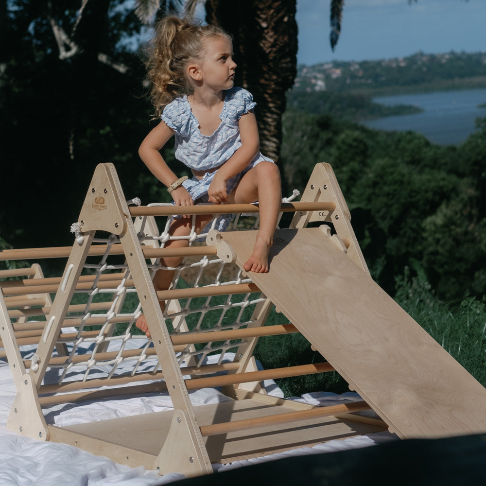 Kind sitzt spielerisch auf dem großen Pikler Dreieck aus Buchen- und Birkenholz, ideal für Spielzeug & Spiele, Montessori Bewegung Kinder.