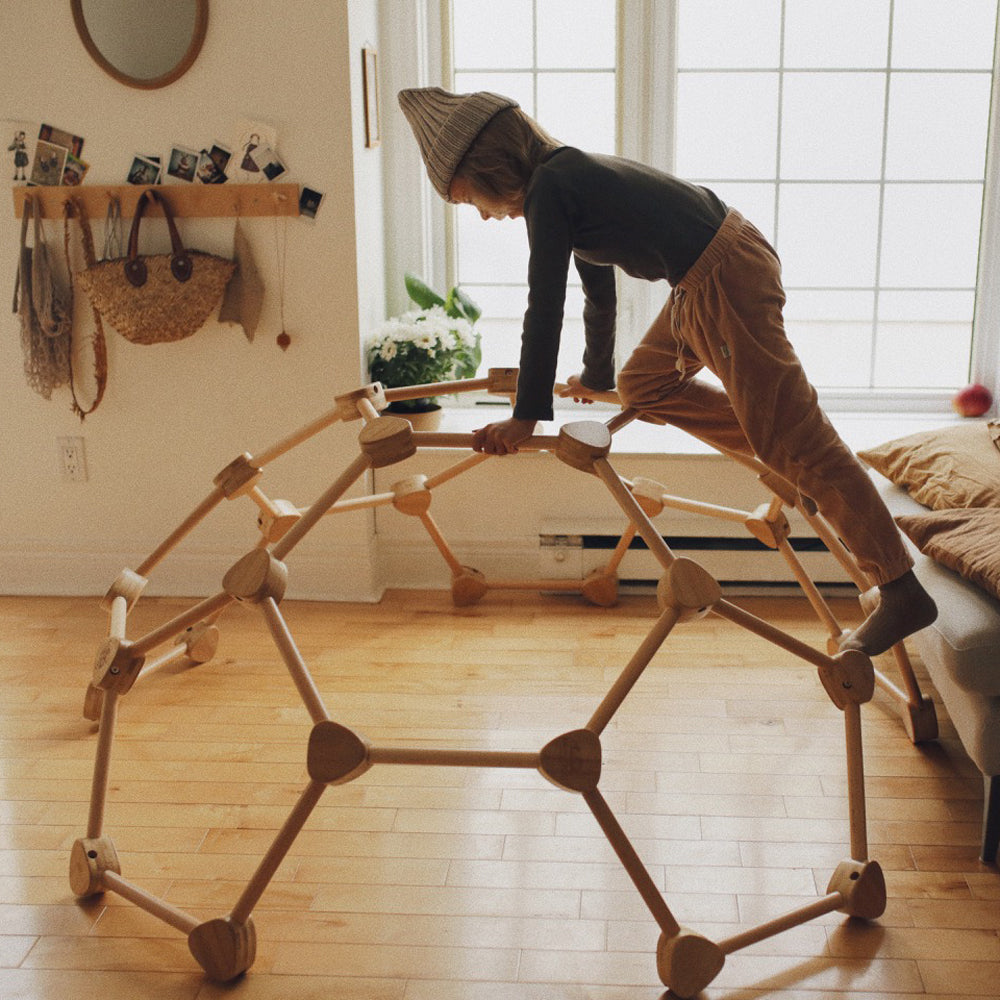 Kind klettert auf natürlicher Pikler Kletterkuppel aus Buche und Bambus, fördert spielerisch Bewegung und Kreativität in Kinderzimmer.