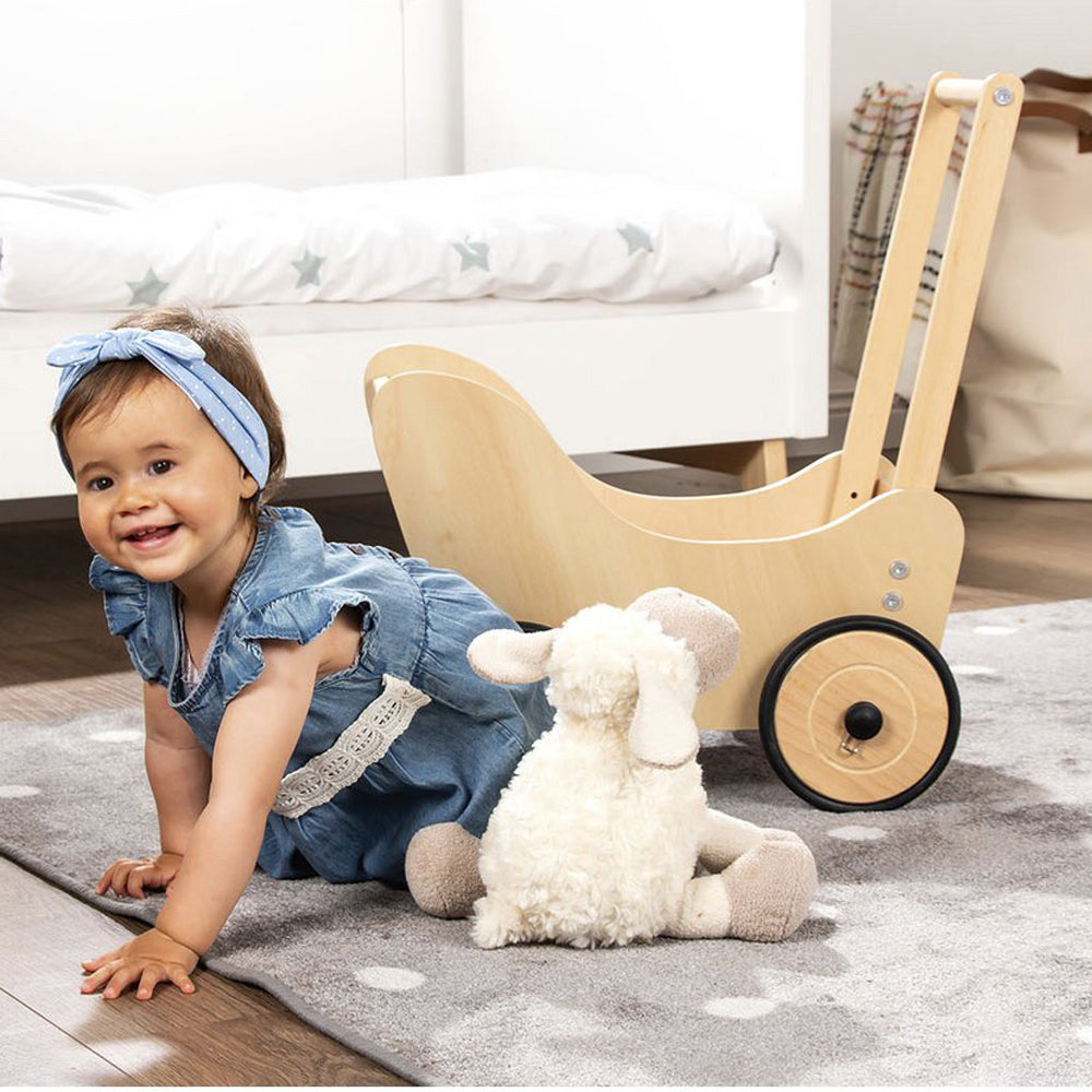 Kleines Kind in Jeanskleid mit Holzwagen zum Puppen- und Lauflernwagen aus Holz mit Bremssystem aus der Kategorie Spielzeug & Spiele.