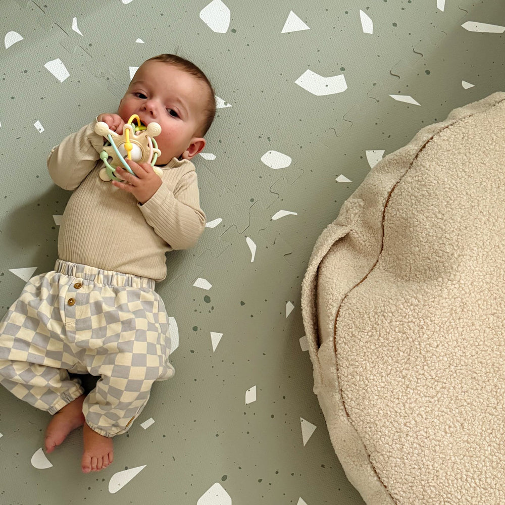 Baby liegt auf Spiel- & Puzzlematte 120x180 cm in Salbei Terrazzo Design, umgeben von weichem Polsterkissen, Spielzeug & Spiele Bereich