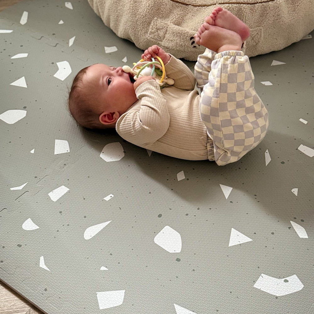 Baby liegt auf Spiel- & Puzzlematte Salbei Terrazzo, ideal für Spielzeug & Spiele sowie Bewegung von Kindern auf weichem Schaumstoffboden.