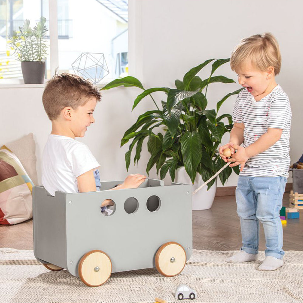 Zwei Kinder spielen mit einer Aufbewahrungskiste auf Rollen mit Deckel im Kinderzimmer neben Pflanzen und Spielsachen.