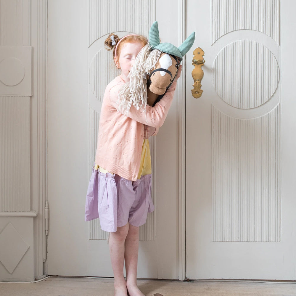 Mädchen umarmt ein beiges Steckenpferd mit offenem Mund aus der Spielzeug & Spiele Sammlung, ideal für Hobby Horsing und Bewegungsspiele.