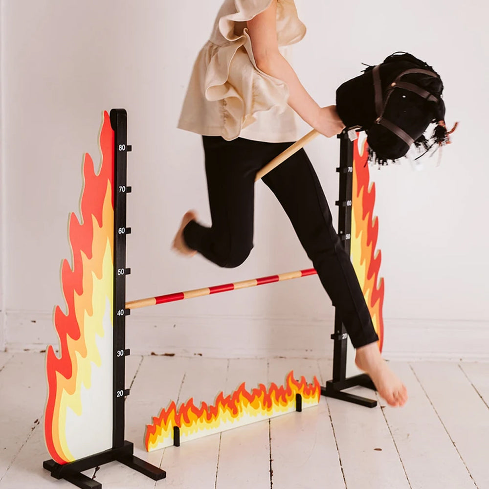 Kind mit schwarzem Steckenpferd springt über Hindernis mit Flammenmotiv aus der Spielzeug & Spiele Tierwelt Themenwelt Sammlung.