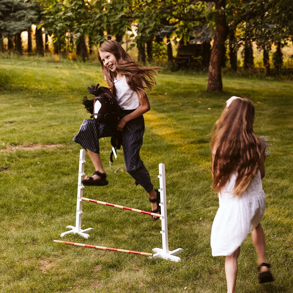 Mädchen spielt mit braunem Steckenpferd offenes Maul beim Springen im Garten aus der Spielzeug & Spiele Sammlung für Kinder.