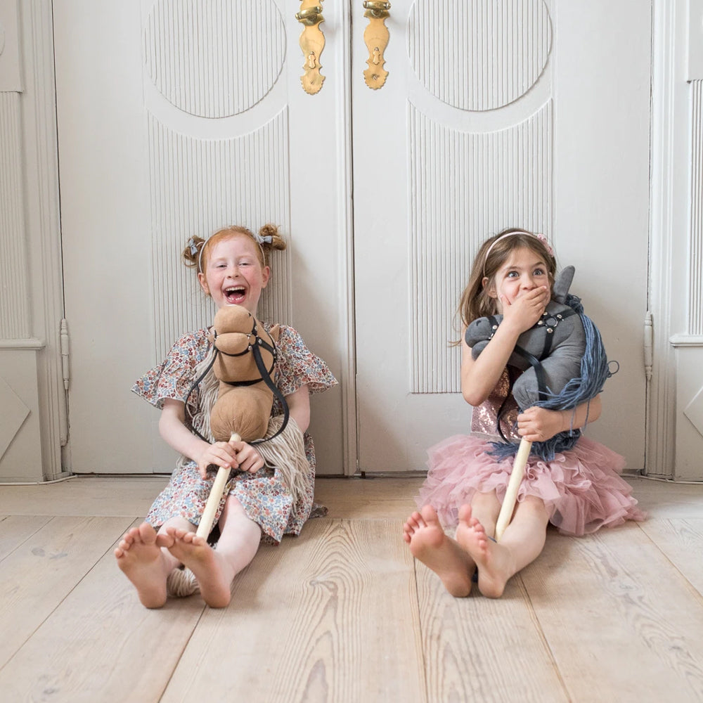 Zwei Kinder sitzen lachend auf dem Boden und halten Steckenpferde mit offenem Maul aus der Spielzeug & Spiele Sammlung.