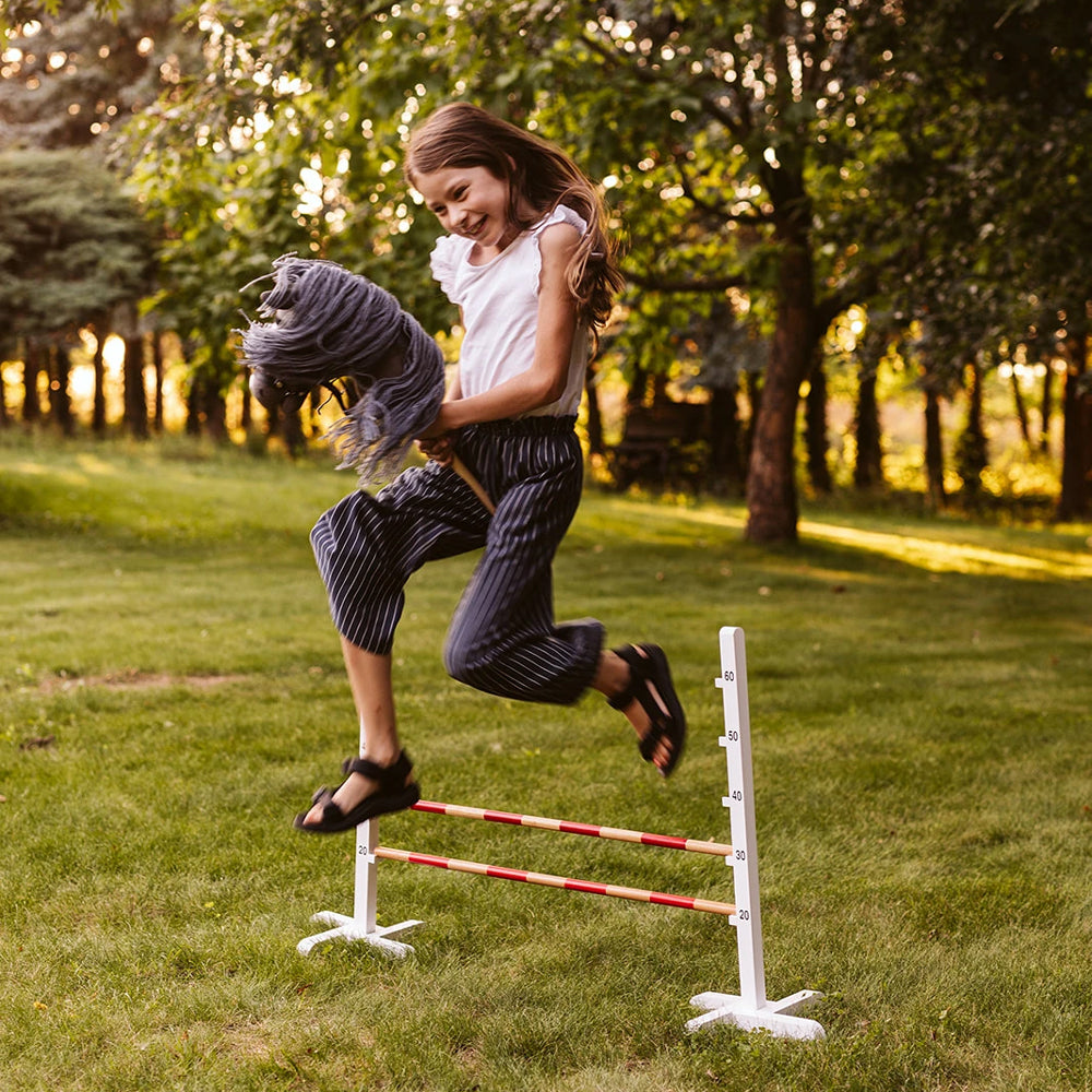 Mädchen springt mit Steckenpferd offenes Maul in grau über Hindernis im Garten aus Spiel & Bewegung Kinder Sammlung.