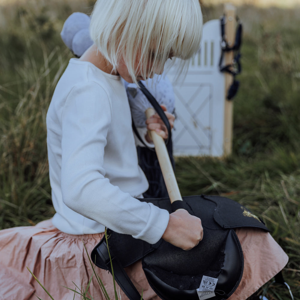 Kind spielt mit grau geflecktem Steckenpferd mit offenem Mund aus der Spielzeug & Spiele Sammlung für Kinder draußen im Gras