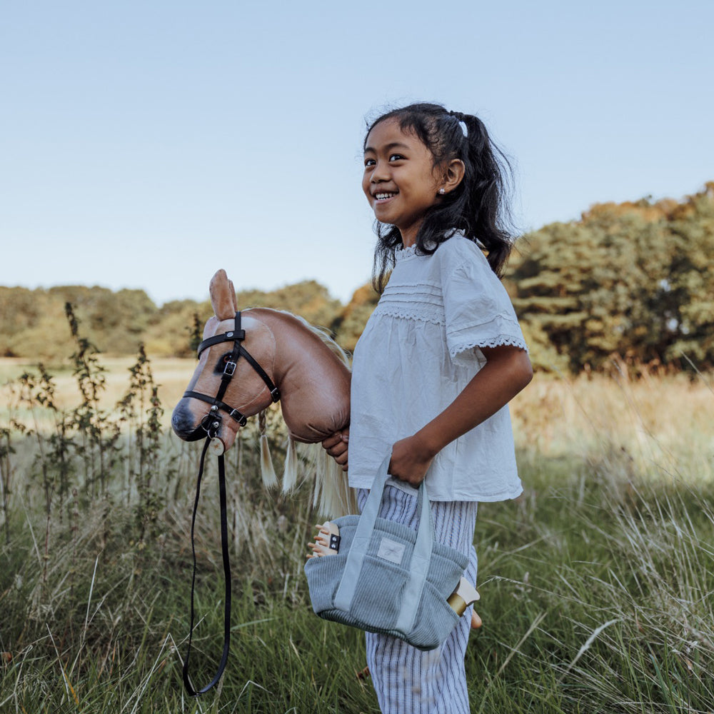 Mädchen spielt draußen mit Steckenpferd Spirit in blond aus der Spielzeug & Spiele Sammlung für Kinder und Hobby Horsing.