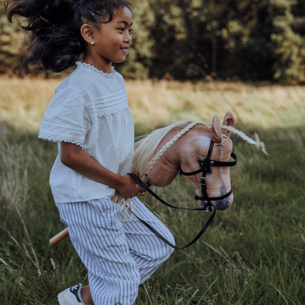 Mädchen spielt mit Steckenpferd Spirit in blond auf einer Wiese aus der Themenwelt Spielzeug & Spiele, Hobby Horsing und Tierwelt.