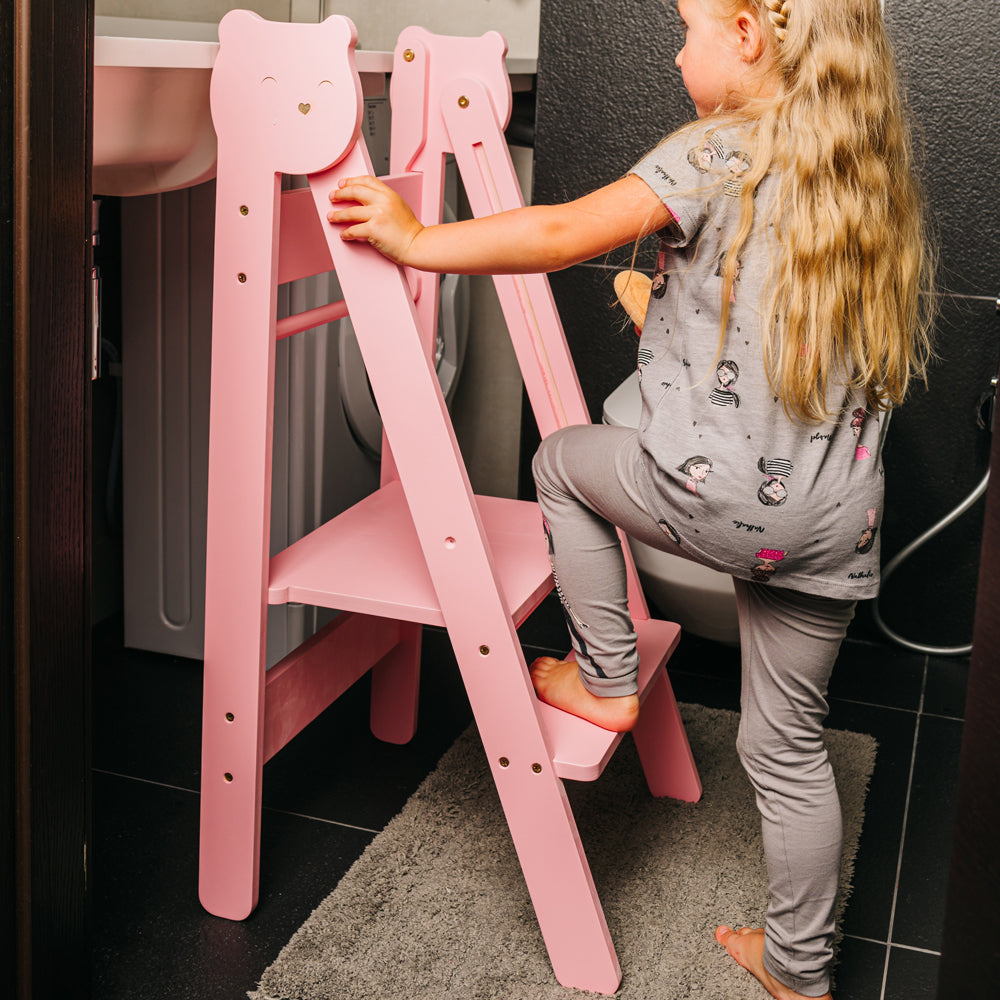 Kind steigt auf rosa klappbaren Tritthocker Lernstuhl mit 2 höhenverstellbaren Stufen im gelben Kinderzimmer Pikler Montessori Stil