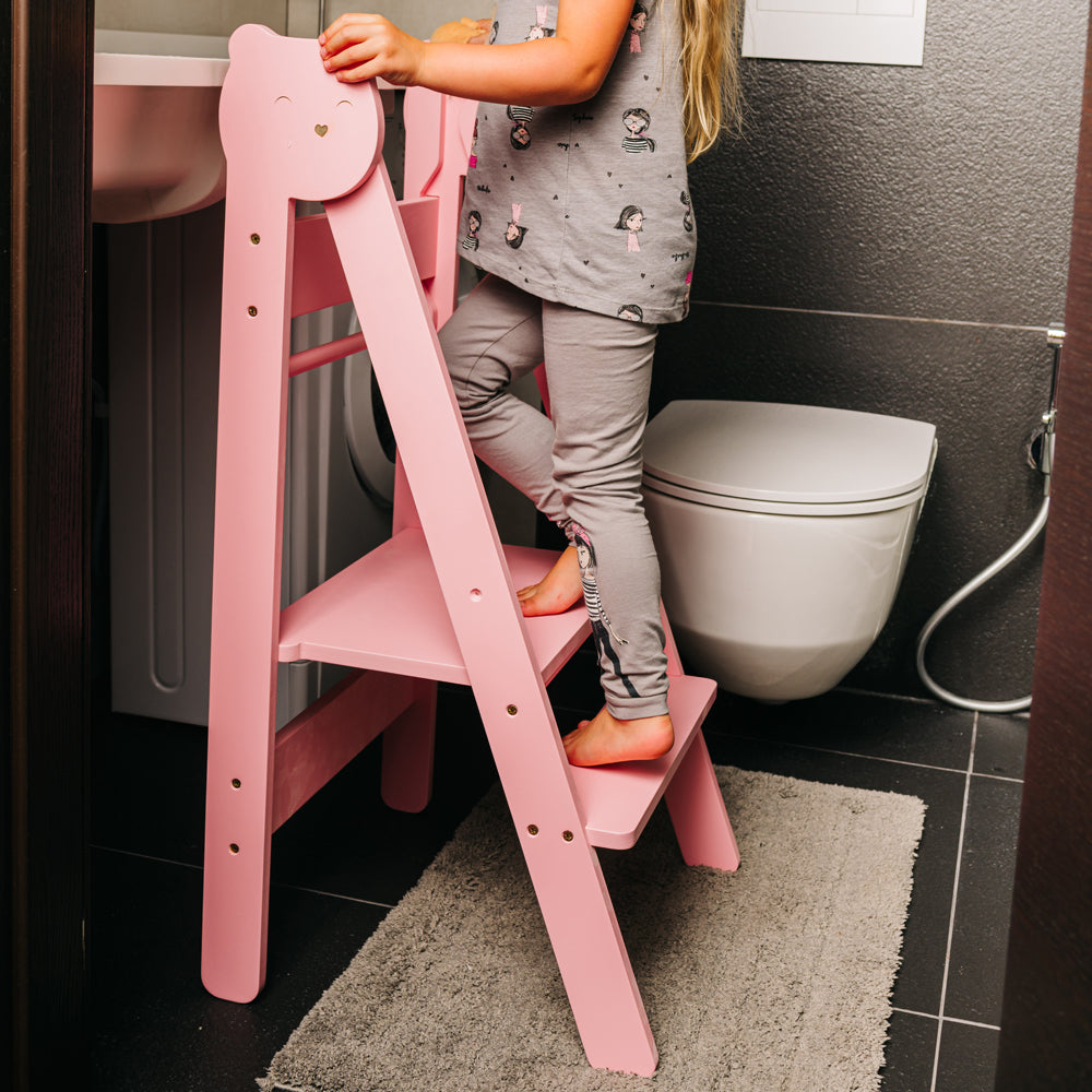 Kind steigt auf rosa Tritthocker Lernstuhl klappbar mit 2 höhenverstellbaren Stufen im gelben Kinderzimmer nach Montessori Prinzip