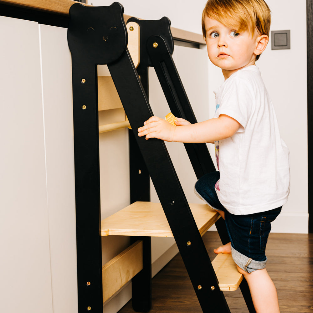 Kind steigt auf klappbaren Tritthocker Lernstuhl mit zwei höhenverstellbaren Stufen im gelben Kinderzimmer nach Montessori Prinzipien.