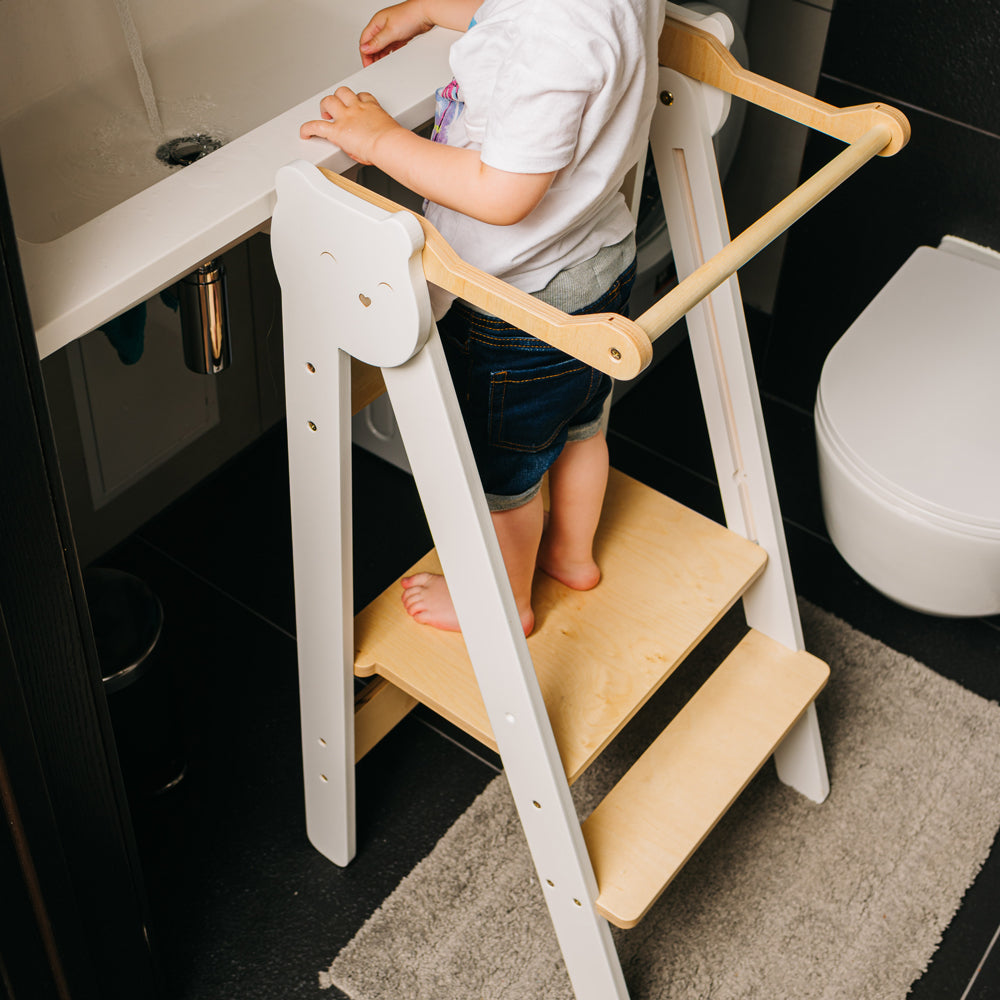 Kind steht auf klappbarem Tritthocker Lernstuhl mit 2 höhenverstellbaren Stufen im gelben Kinderzimmer nach Montessori Prinzip