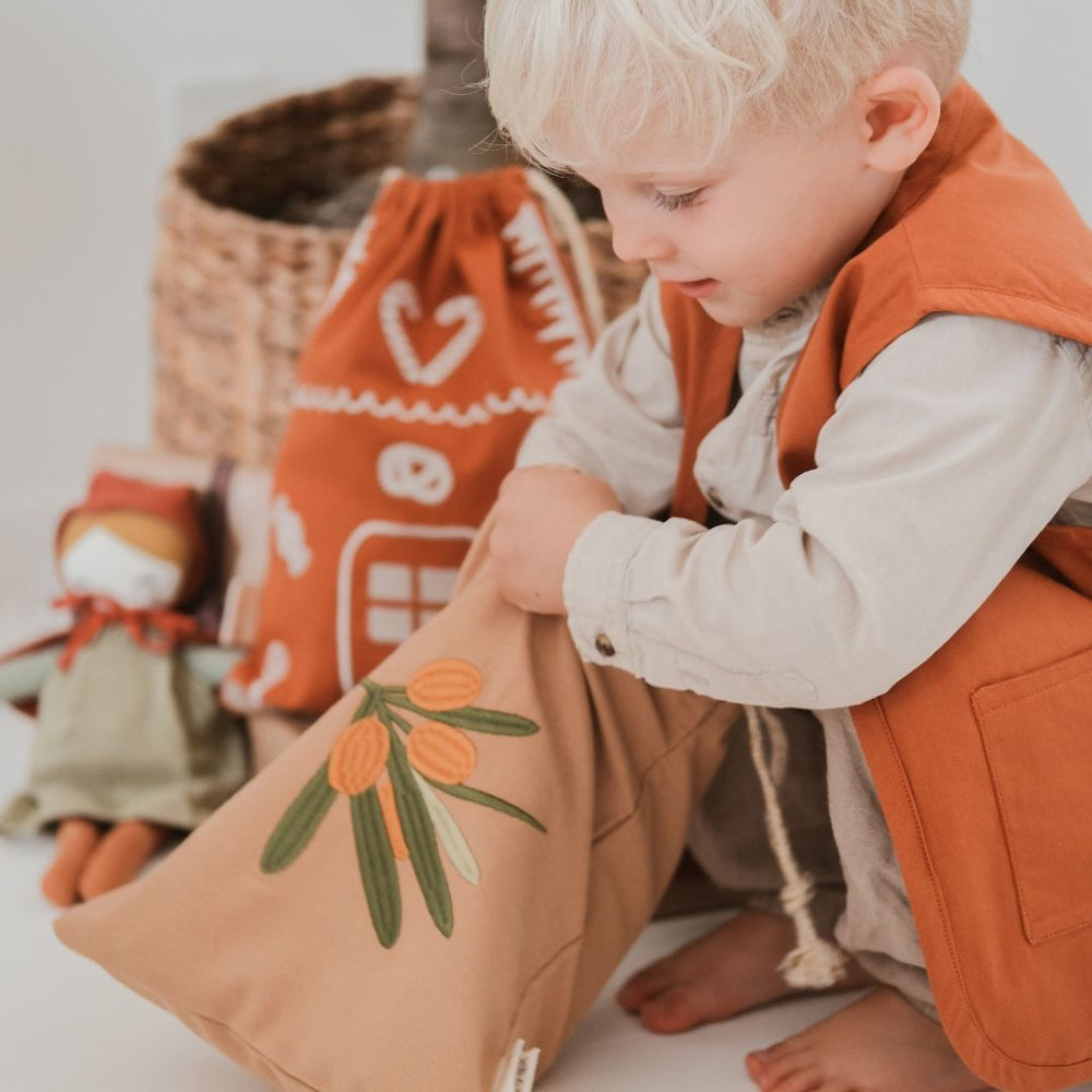 Kleiner Junge betrachtet ein besticktes Weihnachts-Geschenk-Säckchen aus Bio Baumwolle, ideal für Textilien und Accessoires im Kinderzimmer.