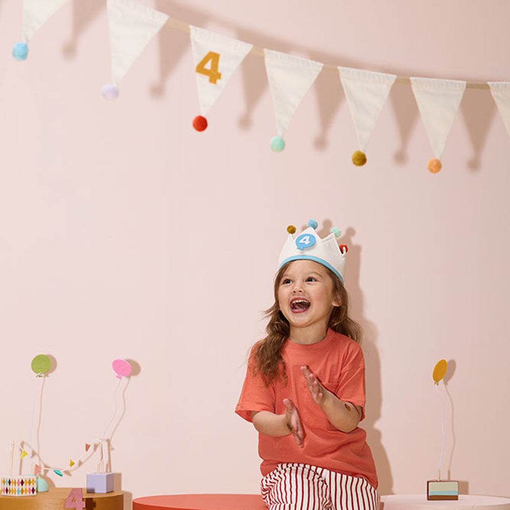 Kind mit geburtstagskrone vor Wimpelkette Pom Pom Girlande mit Zahlen 1-10 als kinderzimmer wanddeko und geschenkidee